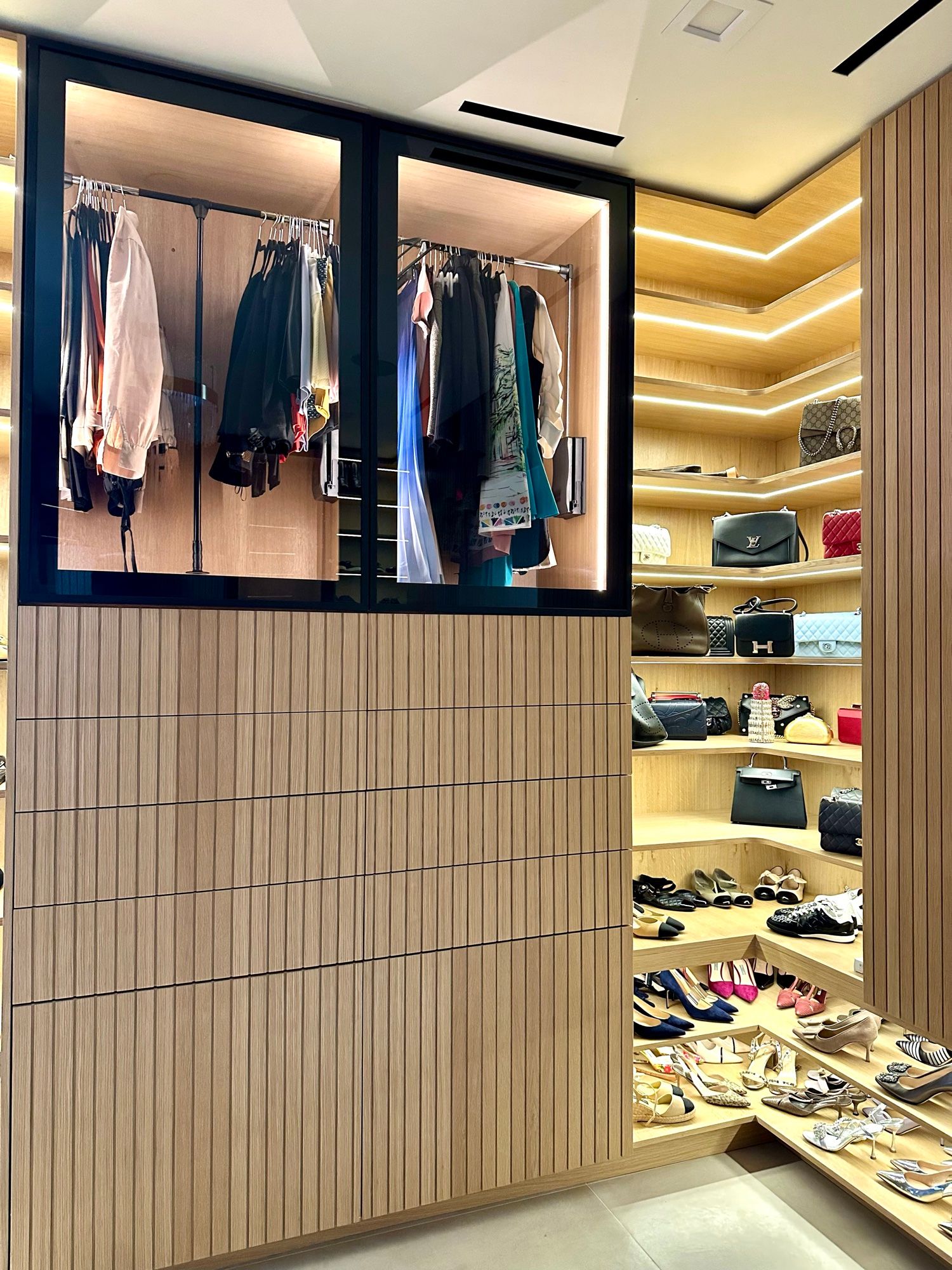 Boutique-style closet with glass display wardrobe and lit shoe shelves