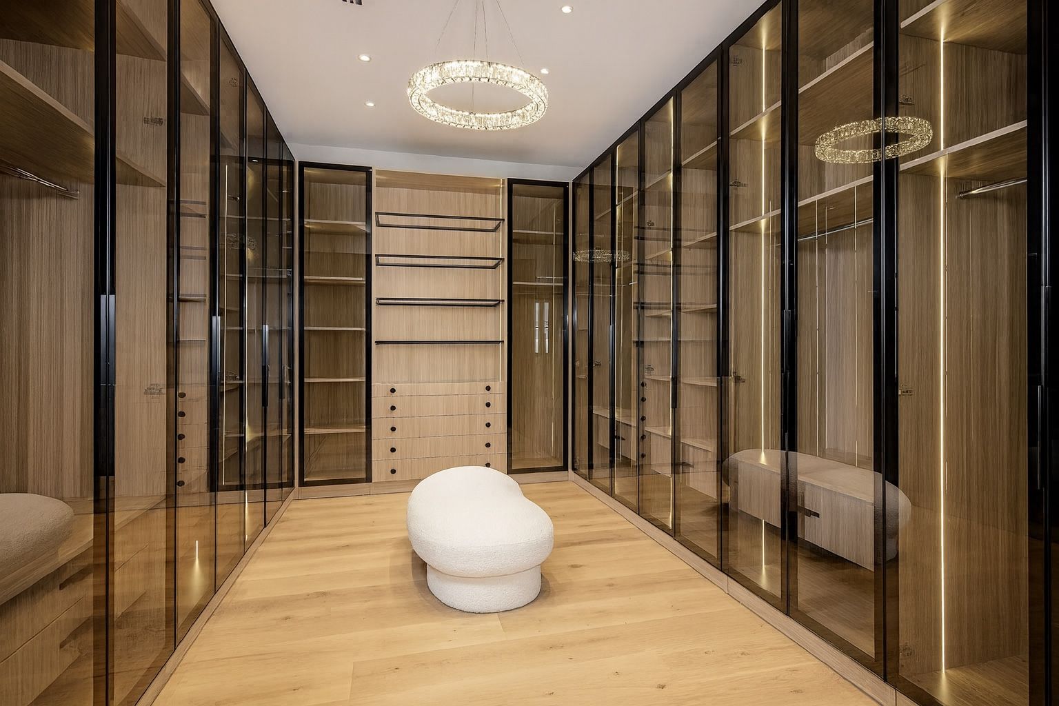 Walk-in closet lined with bronze-framed glass wardrobe doors and a center ottoman