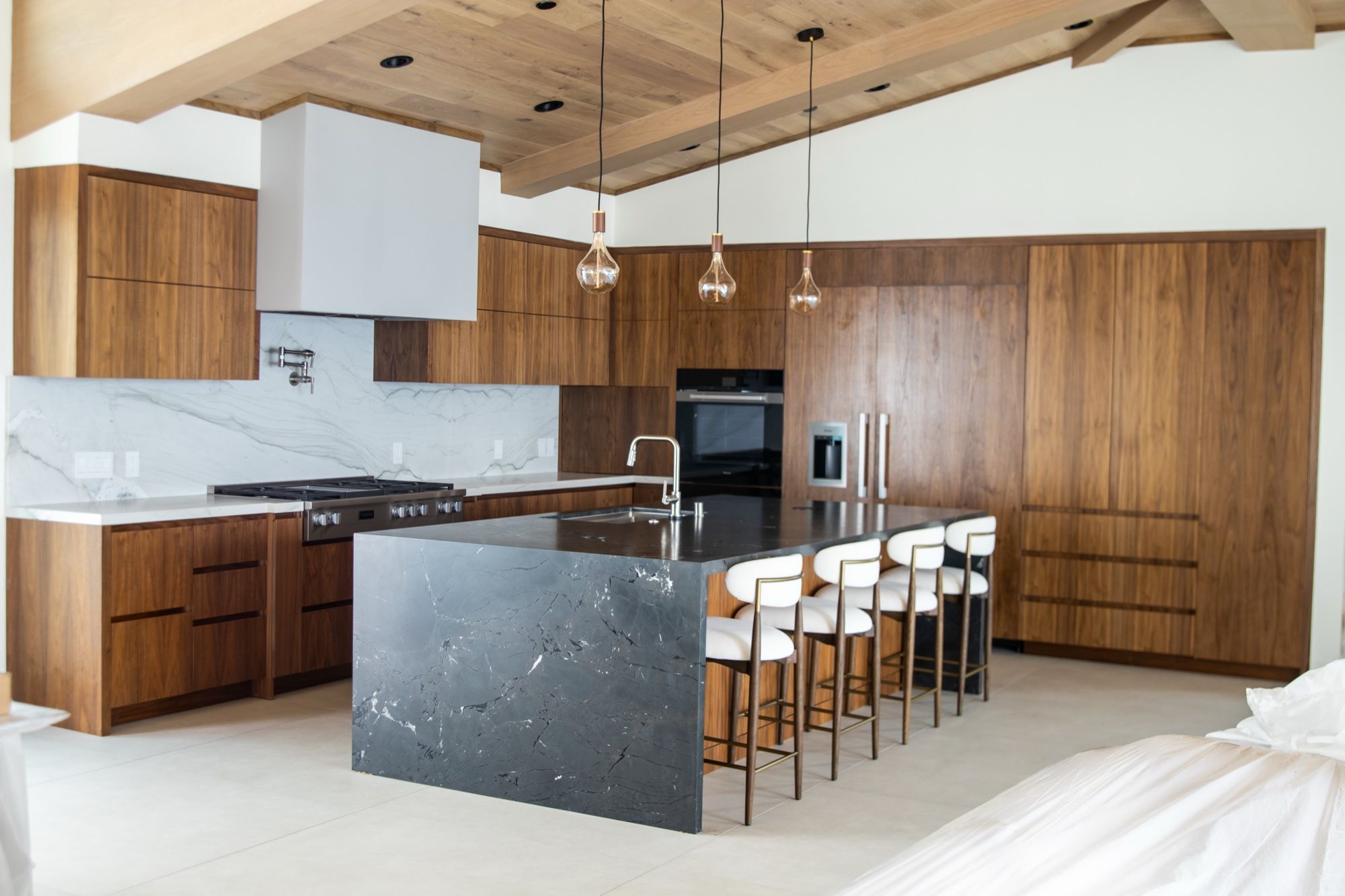 Walnut kitchen with a black marble waterfall island and white counter stools