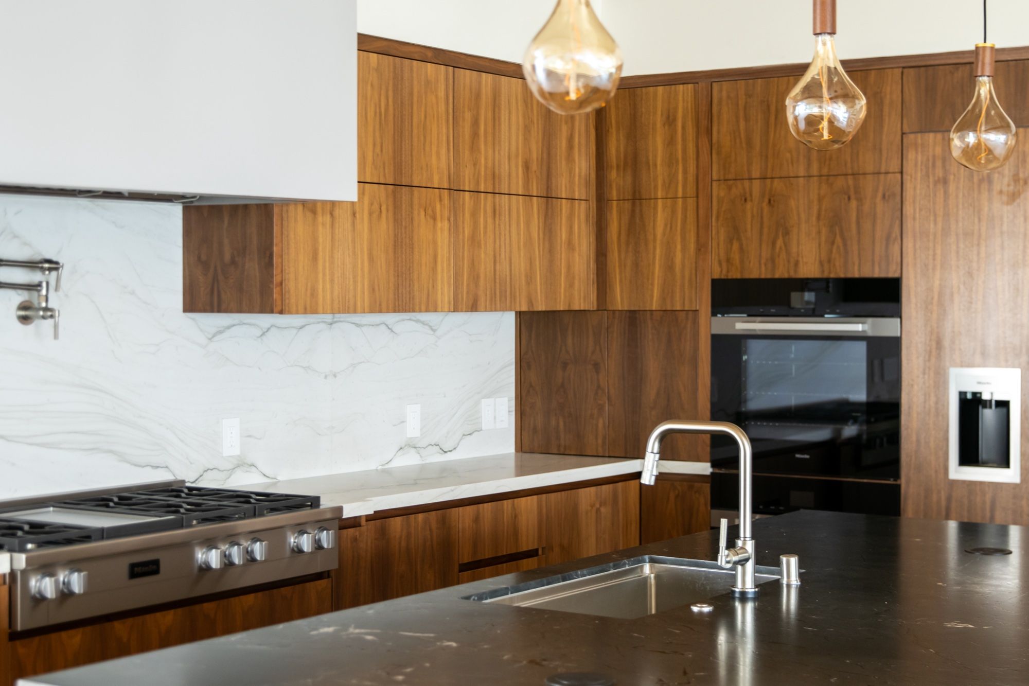 Floor-to-ceiling walnut cabinetry framing a pro range and wall ovens
