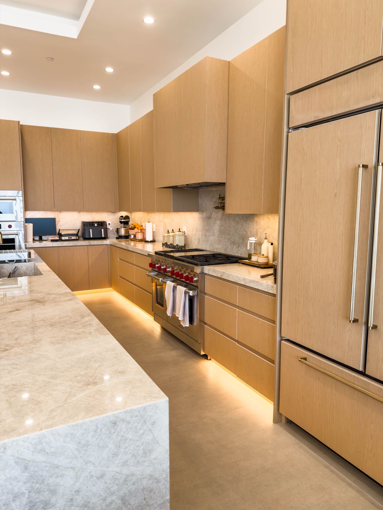 White oak range wall with panel-ready refrigerator and lit base cabinets