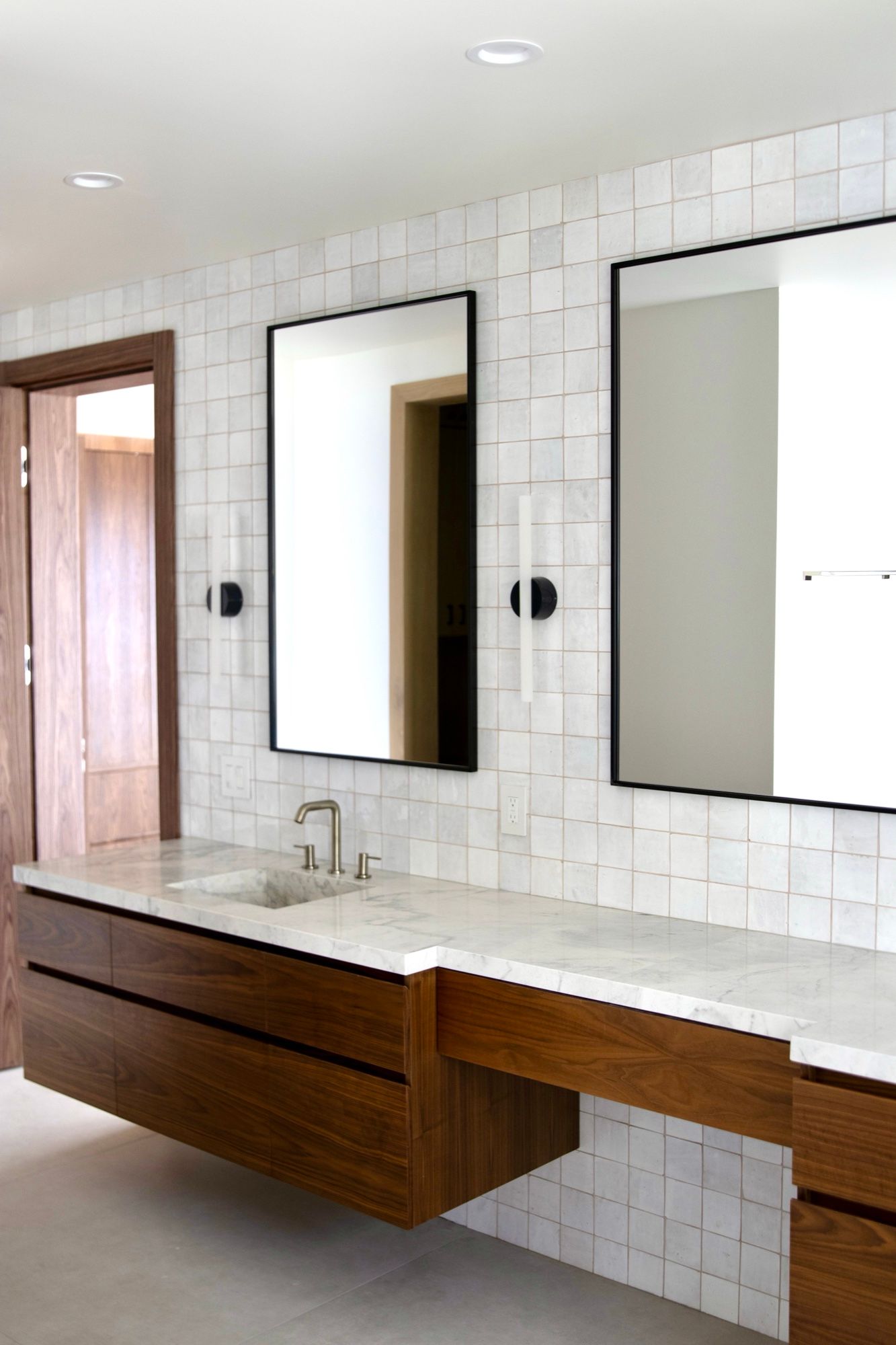 Floating walnut double vanity with black-framed mirrors and white zellige tile