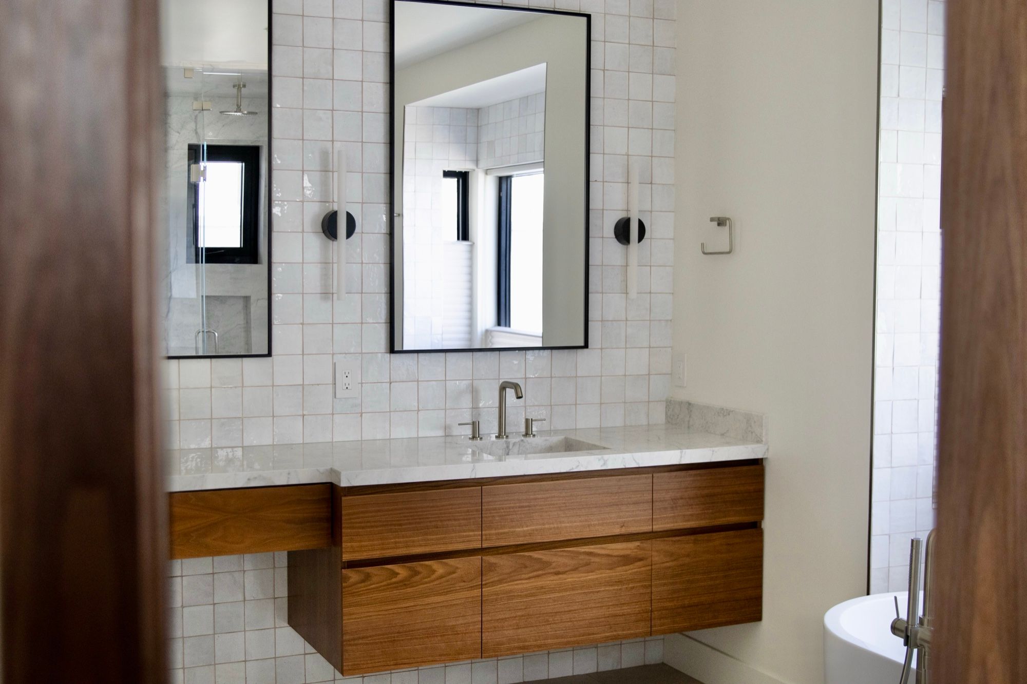Floating walnut vanity with drawers below twin black mirrors